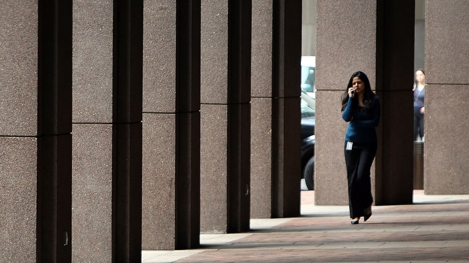 Eine Frau läuft telefonierend vor einem Hochhaus entlang.