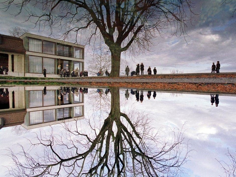 Ein verglastes Gebäude mit einem spiegelnden Teich davor.