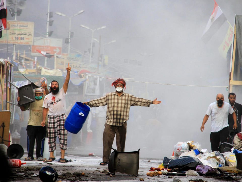 Mursi-Anhänger halten Gegenstände in die Luft und skandieren Parolen. Die Luft ist weiss vom Tränengas.