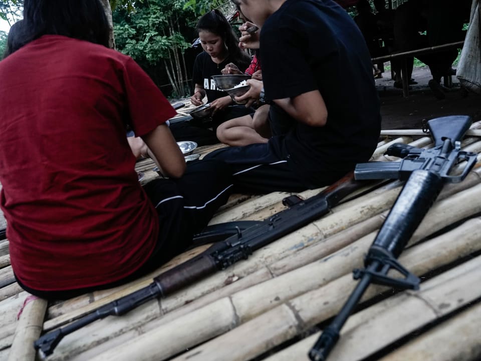 Guerilla-Kämpfer beim Essen, daneben liegen Waffen
