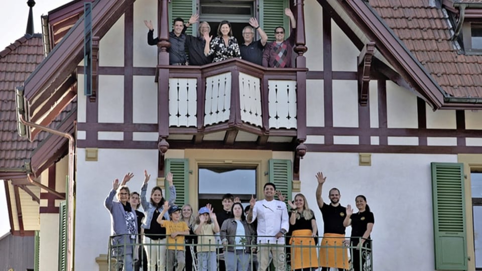 Fachwerkhaus mit Balkon. Davor stehen Jugendliche und ältere Menschen. 