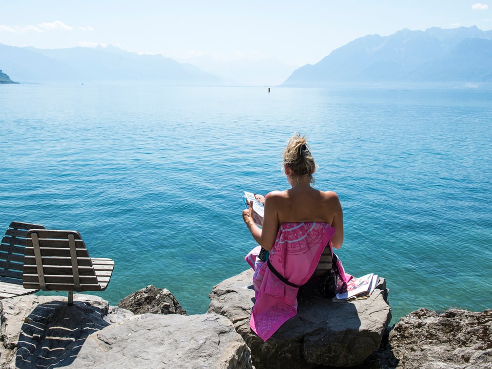 Eine Frau sitzt am Genfersee und liest ein Magazin 