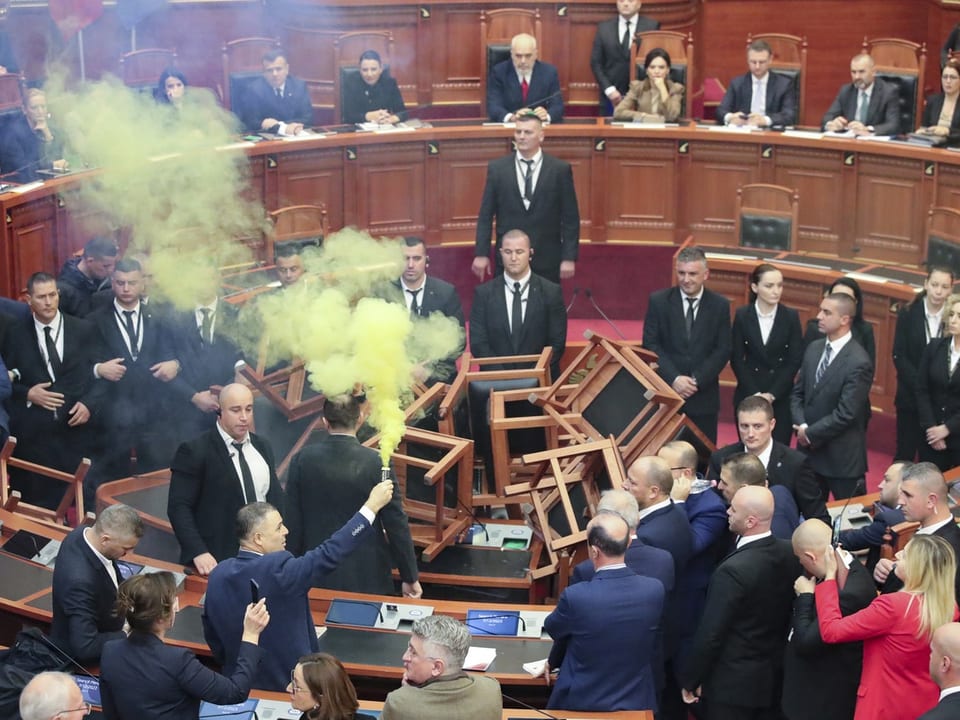 Ein abgeordneter hält eine gezündete Fackel im Parlamentssaal. Gelber Rauch steigt auf. Stühle liegen chaotisch im Saal.