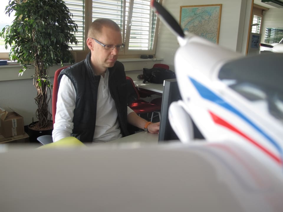 Trüeb sitzt vor seinem Computer, im Vordergrund ein Modell eines Sportflugzeuges.