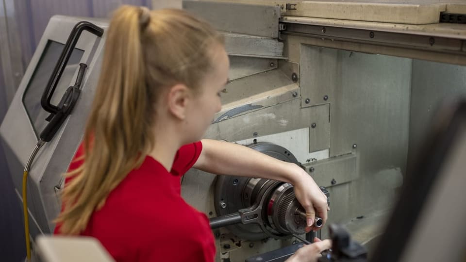 Eine Lernende spannt ein Werkstück in eine Drehmaschine ein.