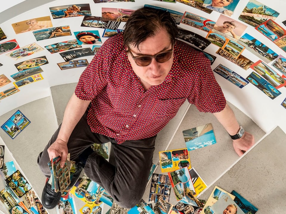 Ein Mann sitzt auf einer Treppe umringt von Postkarten
