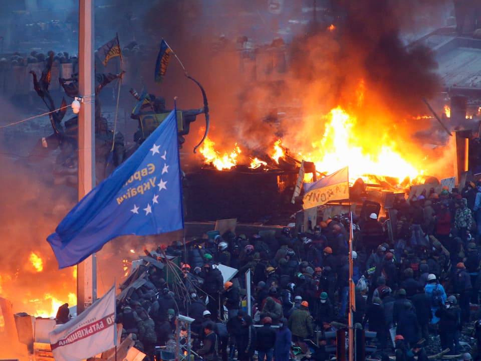 Menschenmassen mit Fahnen und brennende Barrikaden.