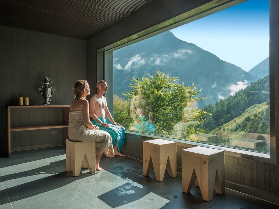 Zwei Personen sitzen in einem modernen Raum vor einem grossen Fenster mit Blick auf Berge