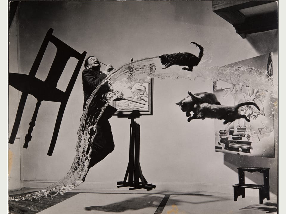Surreale Situation mit fliegendem Stuhl, fliegenden Katzen, einem Wasserstrahl und dem springenden Dali vor einer Staffelei.