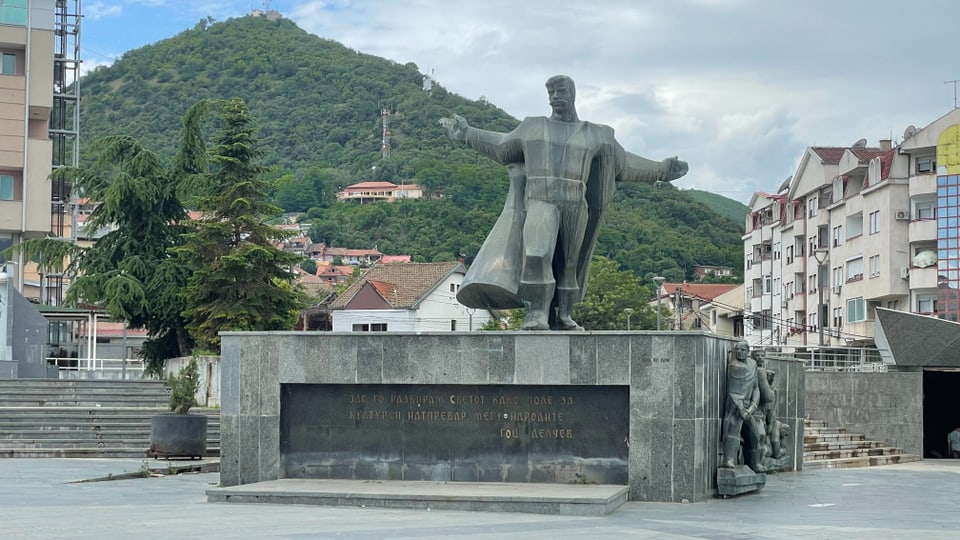 A statue of a man with arms outstretched in front of a wooded hill.