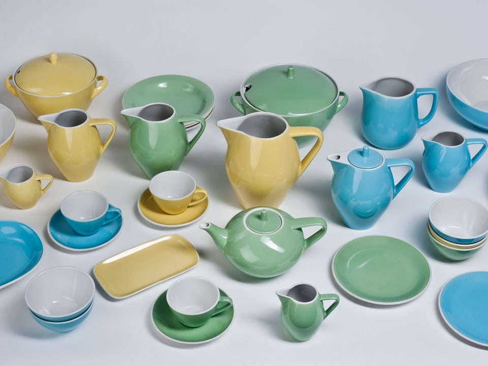 Porzellankrüge, -Teller und -Tassen in grünen, gelben und blauen Pastellfarben.