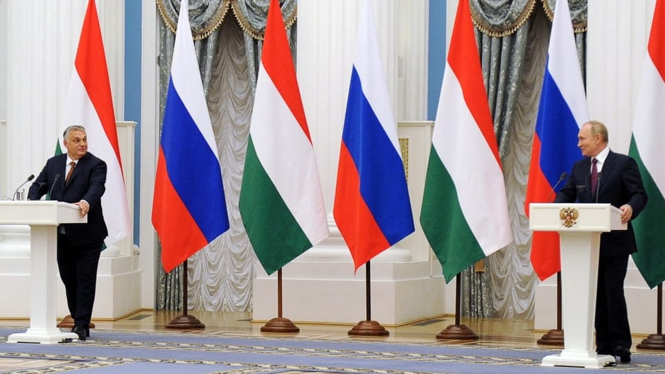 Orbán und Putin stehen weit auseinander und schauen sich an, hinter ihnen sind ihre Landesflaggen.