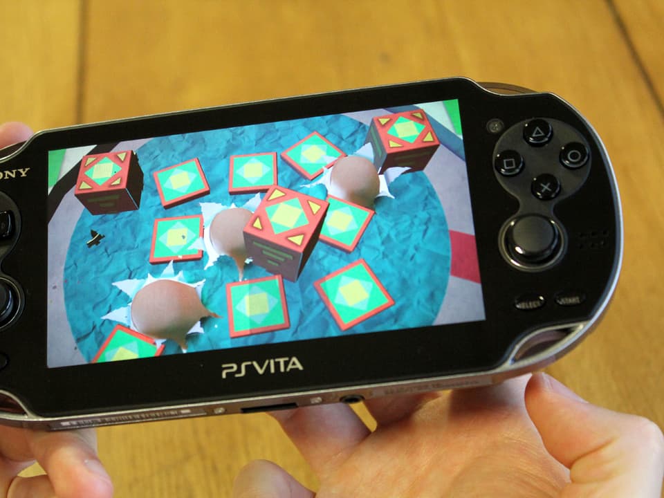 Bild einer Playstation Vita auf der im Spiel «Tearaway» die Fingerspitzen des Spielers durch die Rückwand des Geräts ins Spiel hineinzuragen scheinen