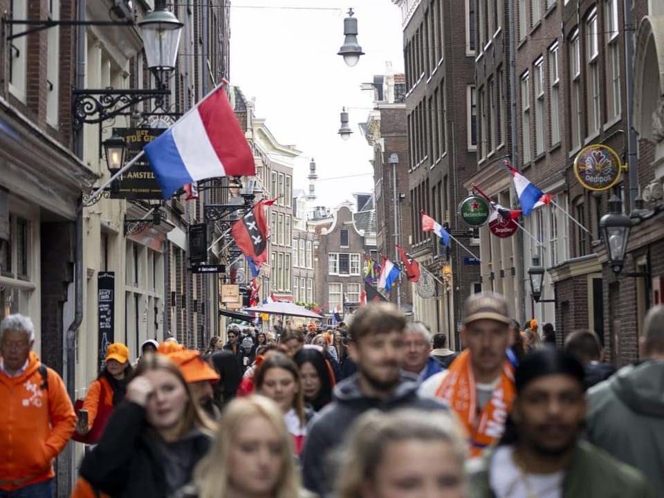 Menschenmenge in einer engen Strasse mit niederländischen Flaggen und anderen internationalen Fahnen