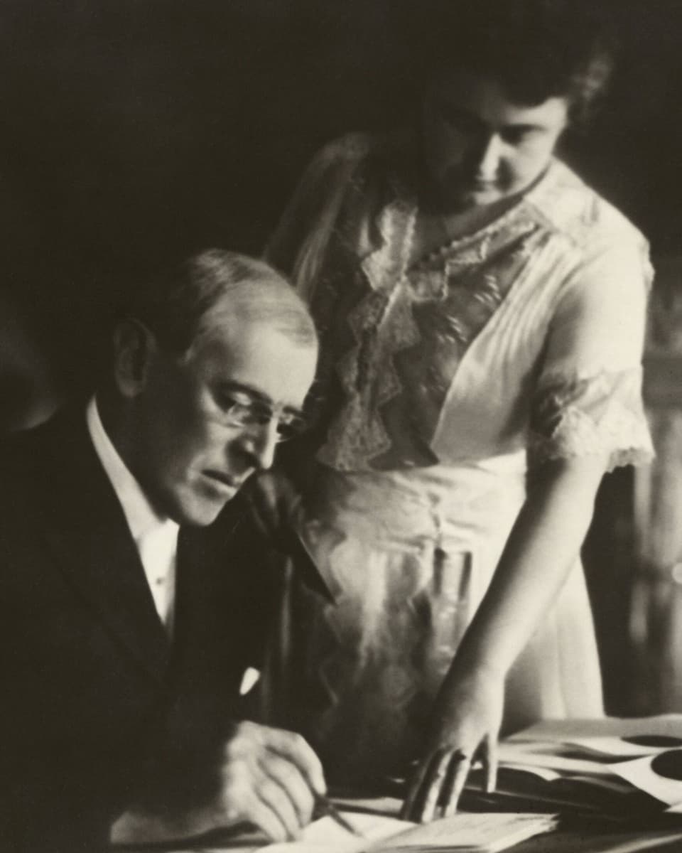 Wilson am Schreibtisch sitzend und seine Frau, Edith Wilson, hinter ihm stehend.