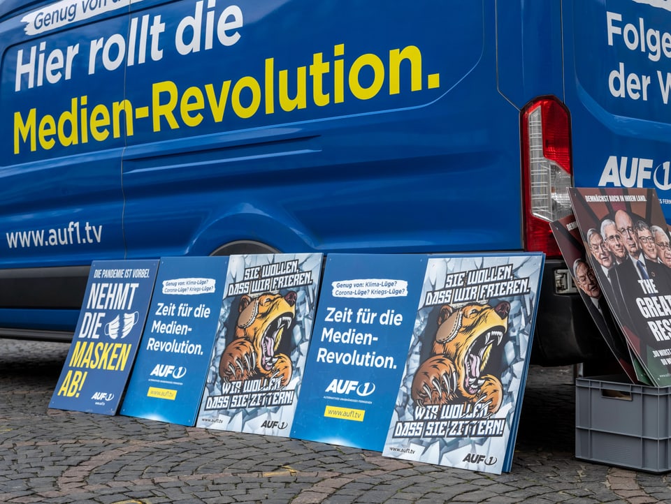 blauer Lieferwagen mit Slogan «Hier rollt die Medien-Revolution», davor Plakate u.a. mit «Wir wollen, dass sie zittern!»