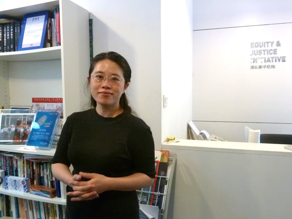 Eine junge Frau steht in einem weissen Büro, im Hintergrund steht ein Bücherregal. 