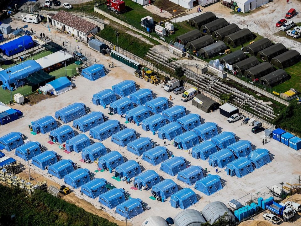 Luftaufnahme: Blaue Zelte in Reih und Glied auf einem Platz.
