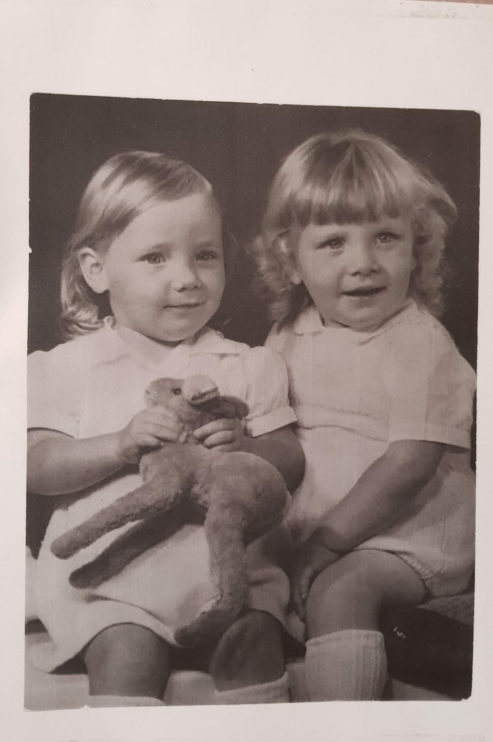 Zwei kleine Zwillinge auf einem Schwarz-Weiss-Foto mit einem Stofftier in der Hand.