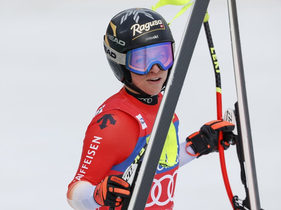 Skifahrer in rotem Anzug hält Skier über der Schulter