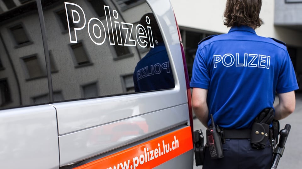 Polizist der Luzerner Polizei neben einem Streifenwagen.
