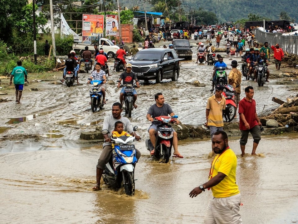 Einwohner der Stadt Sentani fahren auf Motorrädern durch fusshohe Wassermassen. Einige Anwohner laufen durch die Wassermassen.
