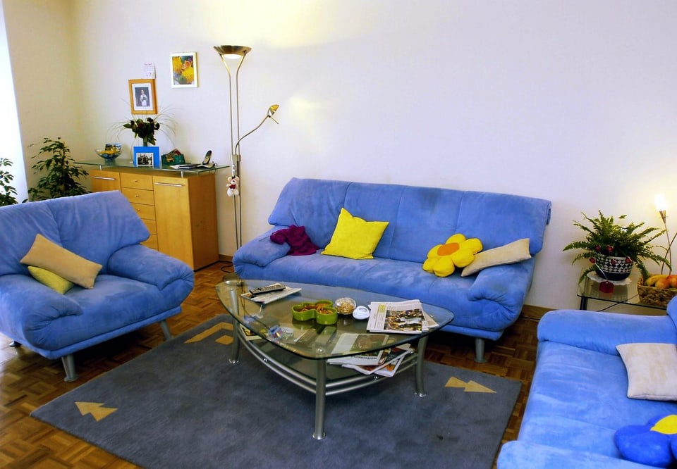 Wohnzimmer mit drei blauen Sofas, einem Teppich und einem Salontisch.