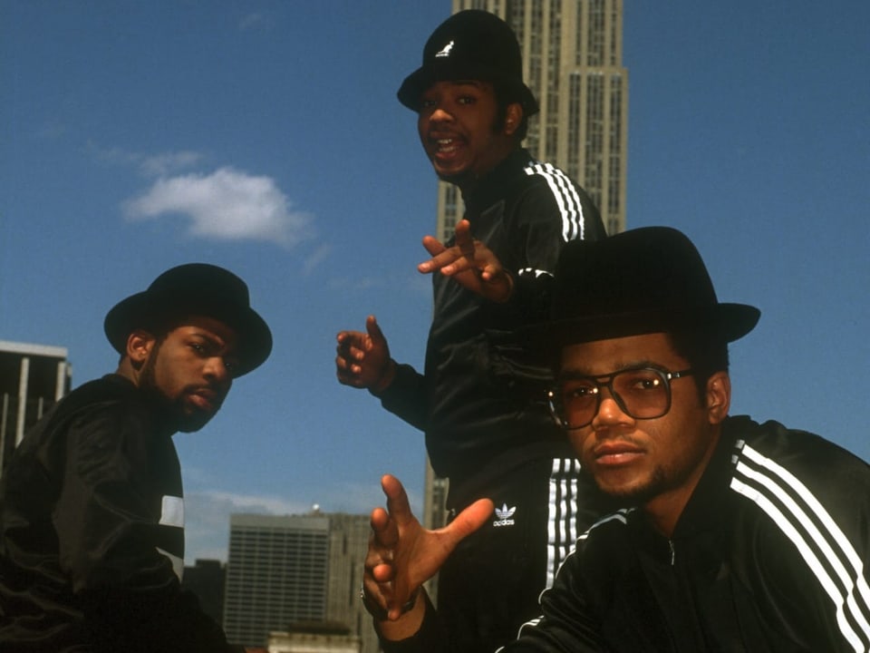Drei junge Männer posieren in schwarzen Trainingsanzügen vor einem Hochhaus