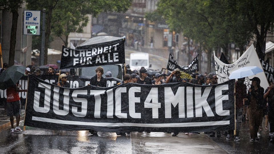Dutzende Personen ziehen mit Banner «Justice 4 Mike» durch die Strassen. Es regnet.