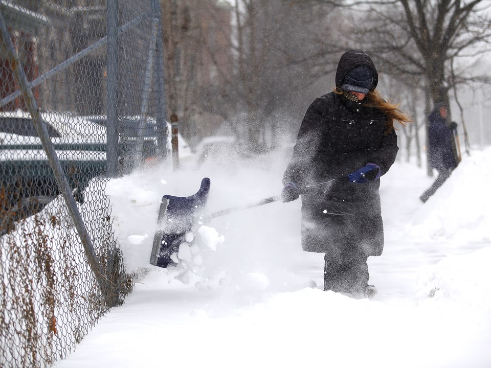 Eine in einen schweren Mantel gehüllte Frau befreit einen Gehsteig in Detroit mit einer Schneeschaufel von den Schneemassen.
