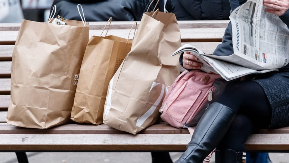 Frau mit Einkaufstüten, Zeitung lesend auf einer Bank