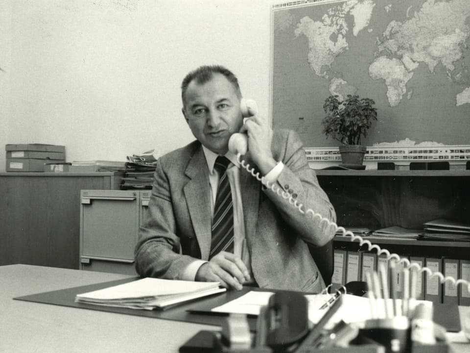 Schwarz-Weiss-Fotografie mit dem Reiseberater, der während eines Telefongesprächs hinter seinem Schreibtisch sitzt.