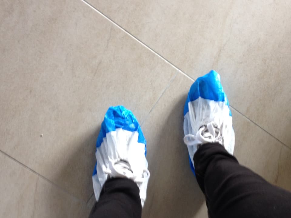Eine Besucherin des MCS-Hauses trägt Plastik-Überzüge an den Schuhen