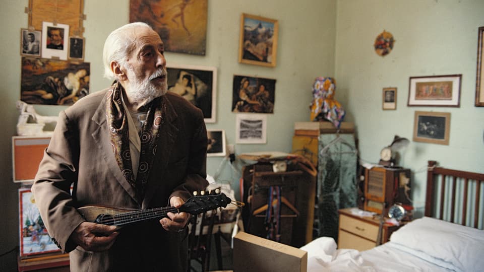 Ein alter Mann mit Gitarre in seinem Altersheim Zimmer.