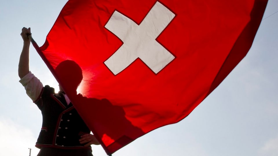 Ein Schwinger hält die Schweizer Fahne, die im Wind flattert-