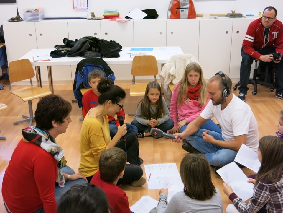 Teubers Kinder in einer Mehrklassen-Klasse. Die Kinder und Lehrpersonen sitzen in einem Kreis am Boden.