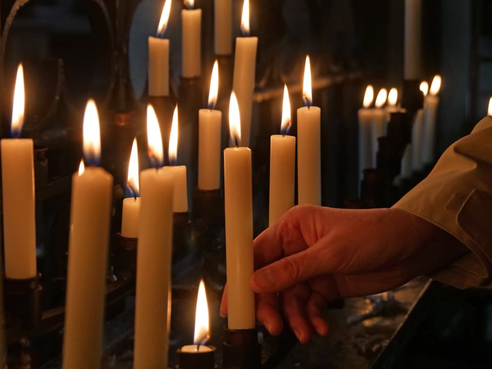 Hand berührt Kerzen in einer Reihe auf einem Kerzenständer in einem dunklen Raum.