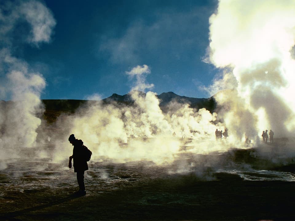 Mann steht an einer Quelle in der Atacamawüste. Es dampft um ihn herum.