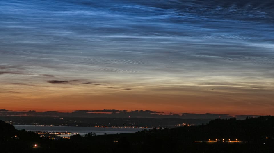 Blick zum Bodensee, darüber das Abendrot mit dunklen Cirren, darüber die bläulich-weissen Leuchtenden Nachtwolken.