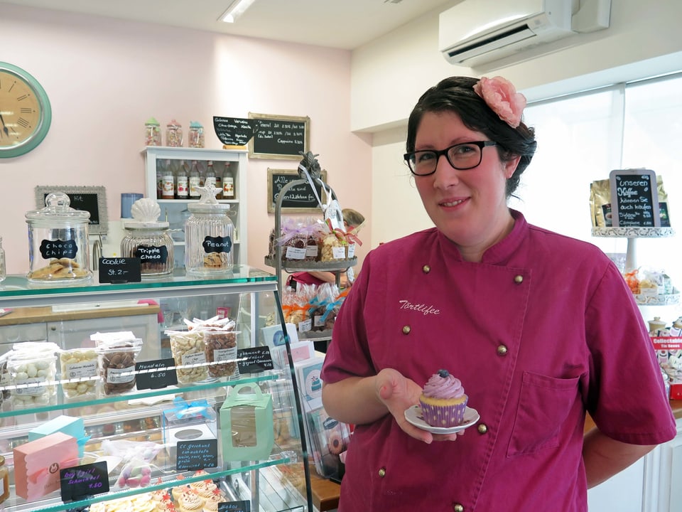 Törtlifee steht mit Muffin in der Hand neben ihrem Verkaufstresen