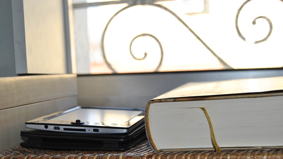 Das Bild zeigt ein dickes Buch und einen E-Reader