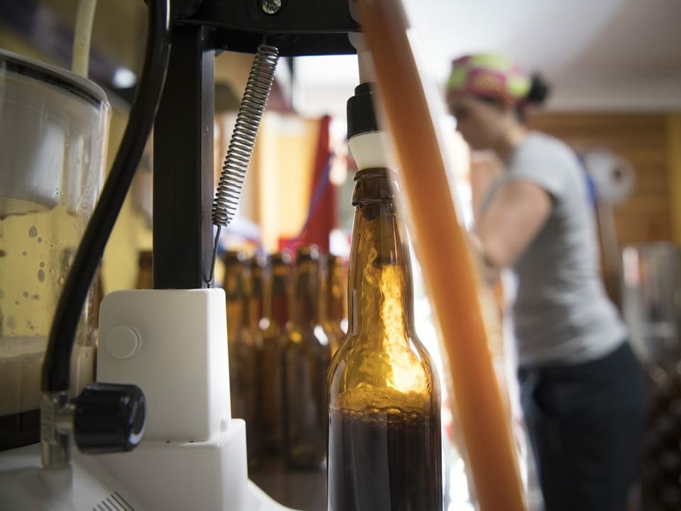 Blick in eine Mikro-Brauerei mit einer Bierflasche im Vordergrund, die gerade gefüllt wird.