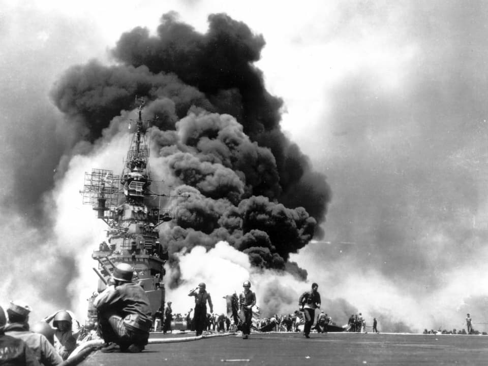 Ein Kriegsschiff und Soldaten sind zu sehen, im Hintergrund eine Explosion, die eine grosse Staubwolke hinterlässt.
