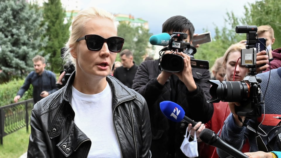 Eine Frau mit Sonnenbrille spricht zu Journalisten