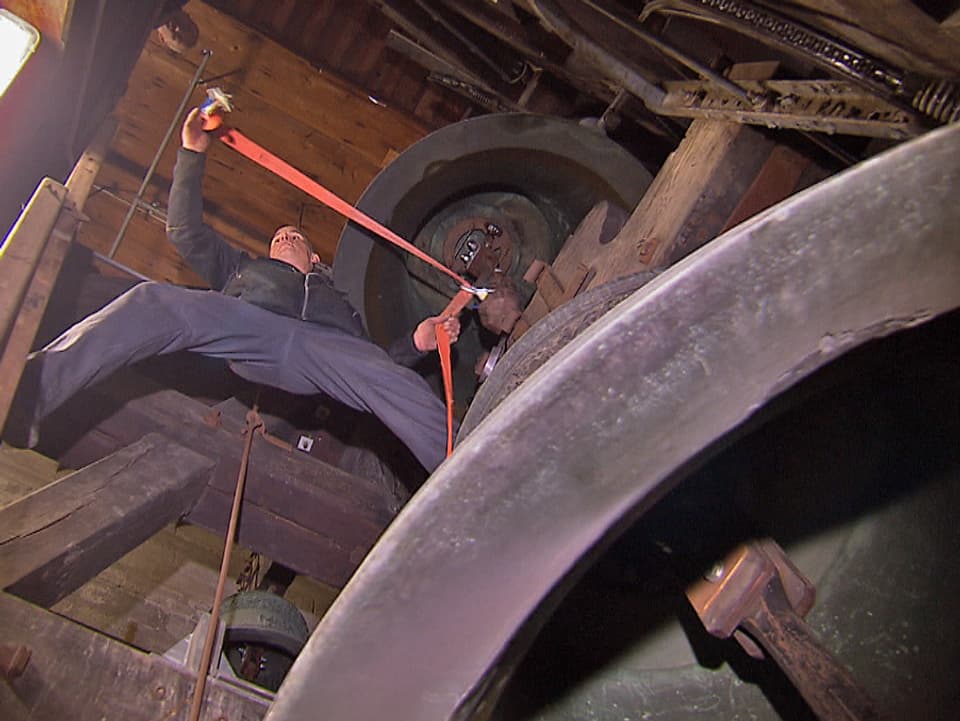Ein Mann befestigt im Glockenturm einen Glockenklöppel.
