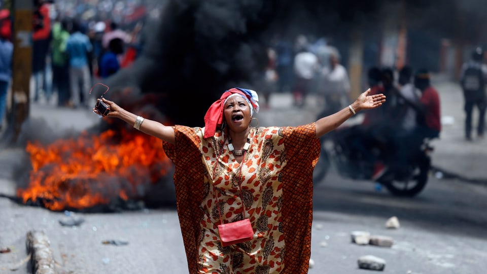 Eine Demonstrantin skandiert Parolen, Reifen brennen im Hintergrund