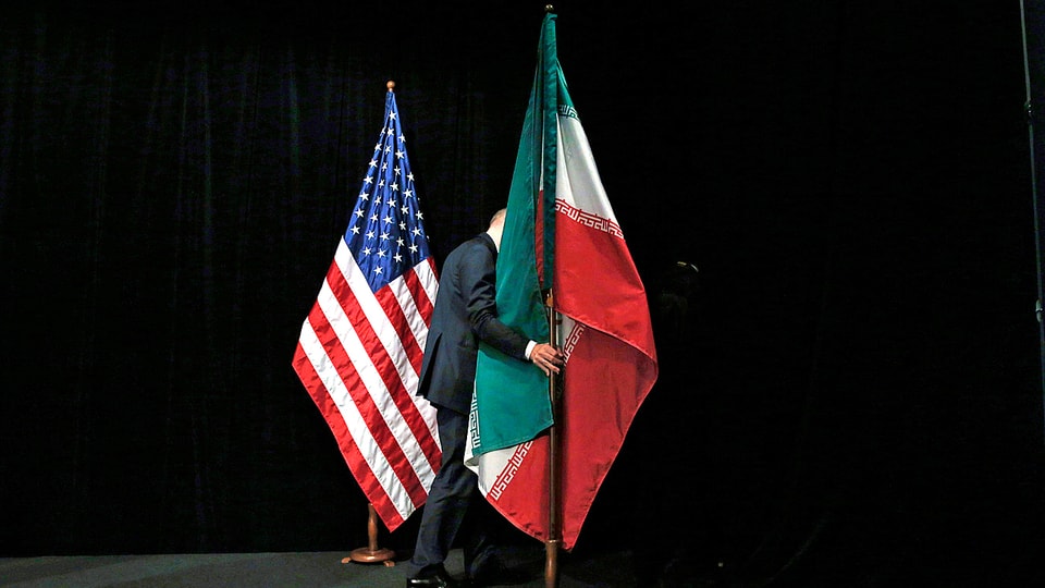 Ein Mann entfernt die Flaggen der USA und jene des Irans von einem Gesprächspodium.