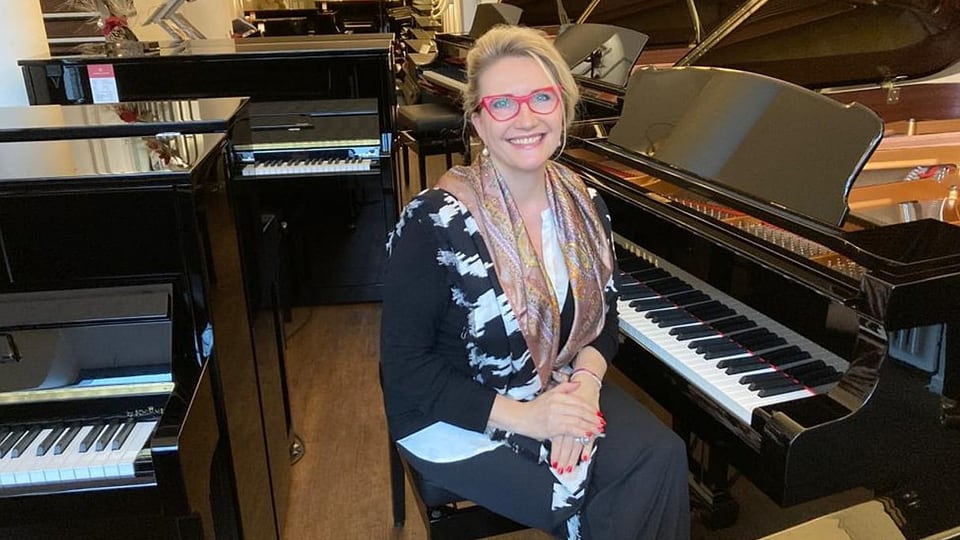 Eine Frau mit Brille sitzt an einem Piano in einem Pianogeschäft.