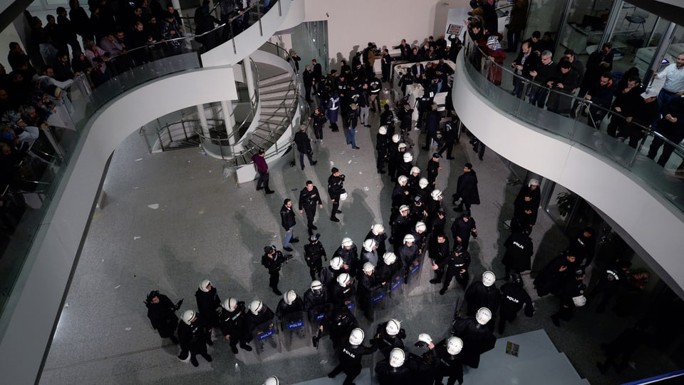 Eingangshalle von oben fotografiert, dort stehen dutzende Polizisten mit weissen Helmen und Schildern.