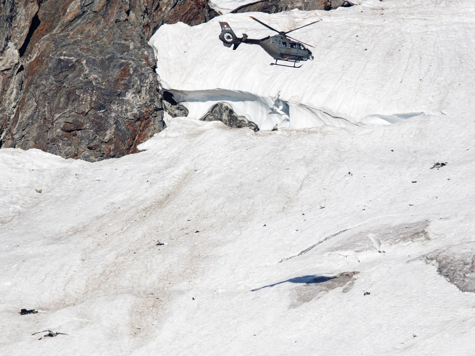 Armeehelikopter überfliegt kleinere Flugzeugtrümmer am Fuss einer Felswand